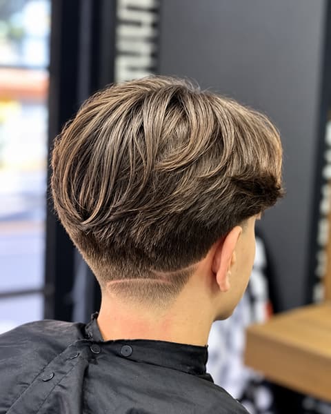 Cabelo liso com volume no topo, nuca baixa no degradê e um risco horizontal