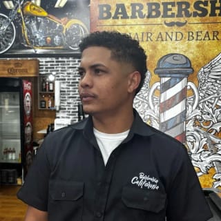 Bahia, de camisa preta da Barbearia Califórnia, em frente ao mural da barbearia