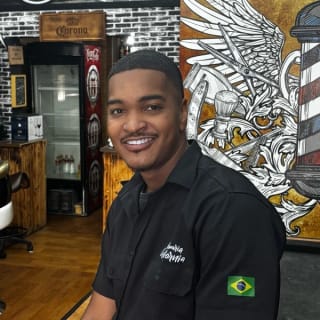 Du sorrindo, de camisa preta da Barbearia Califórnia com bandeira do Brasil na manga