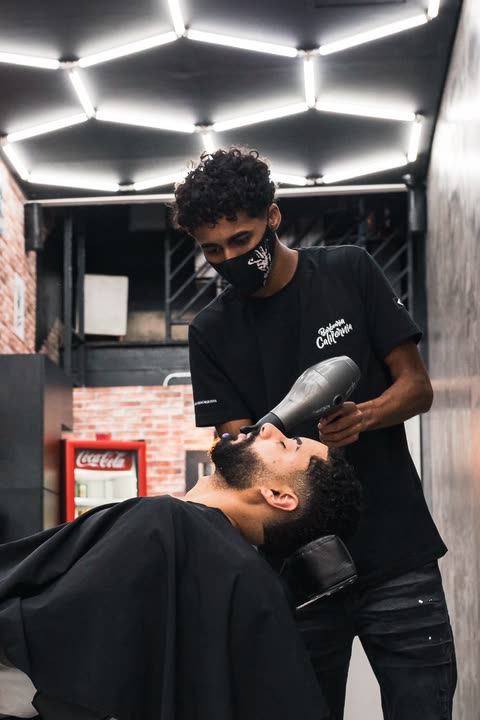 Barbeiro finalizando a barba do cliente com secador